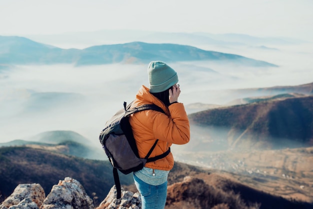 Una chica de senderismo con una mochila en la espalda mira la mañana desde la cima de la montaña.