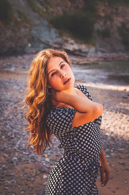 Chica sensual en una cala rocosa con un vestido de lunares blanco y negro