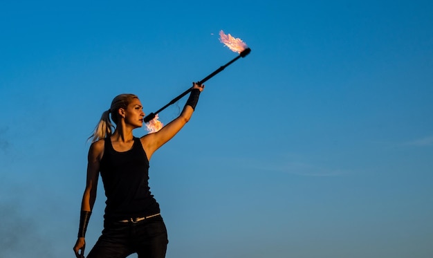 Chica sensual caliente y sexy bastón de fuego giratorio Chica bonita manipular vara llameante al aire libre Intérprete de fuego femenino en el cielo azul Bastón girando Celebración navideña Fiesta nocturna copia espacio