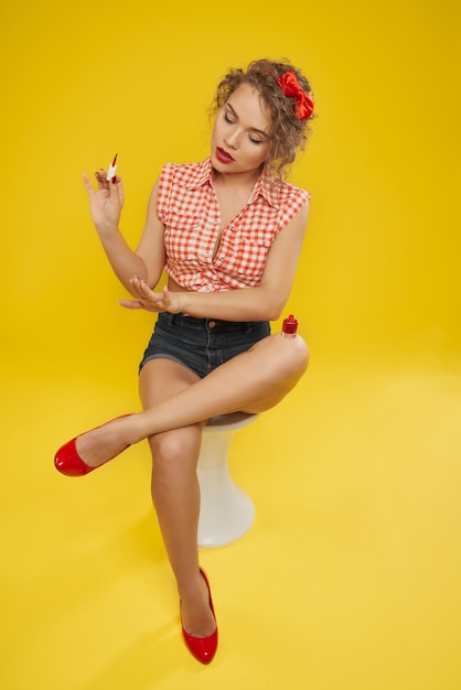 Foto chica sentada y aplicando esmalte rojo para uñas.