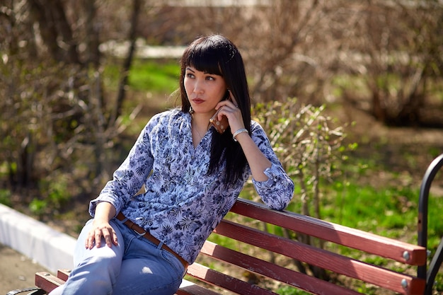 Chica sentada en el banco en el parque y hablando por teléfono.