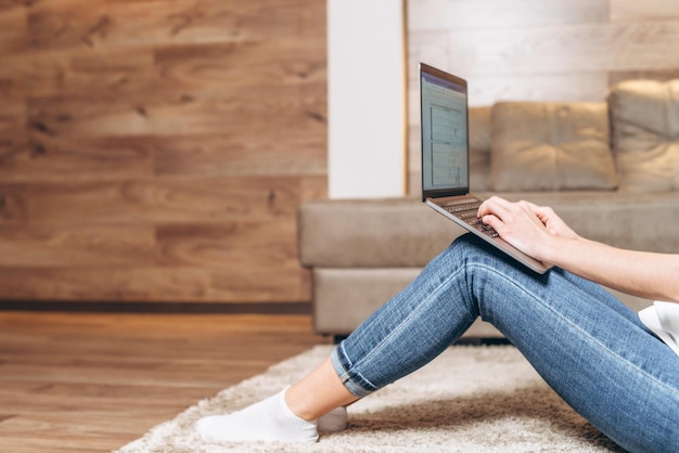 Chica sentada en casa trabajando y navegando en línea en la computadora portátil