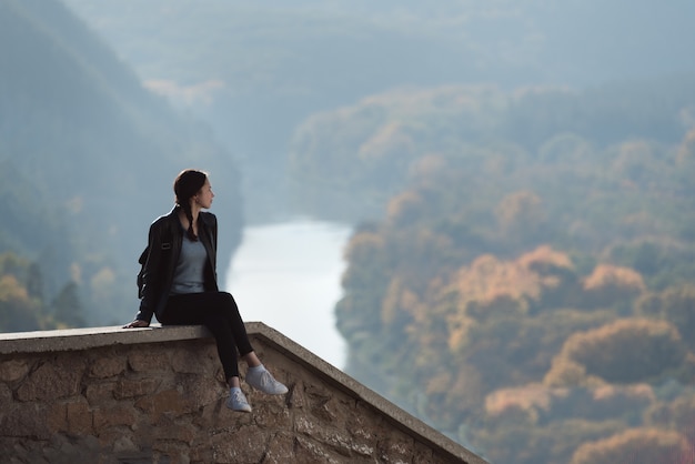 Chica sentada en la colina y mira a lo lejos del bosque y el río.