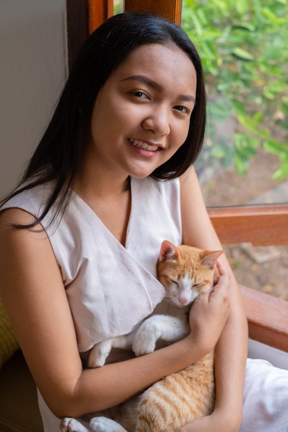 La chica sentada con un gato en la ventana de casa.