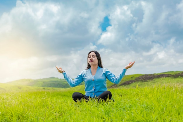 Chica sentada haciendo yoga de meditación en el campo mujer haciendo yoga al aire libre mujer joven haciendo yoga en la hierba en el campo con cielo azul de fondo