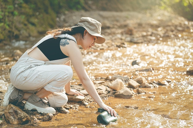 Chica sentada junto al arroyo bebiendo agua