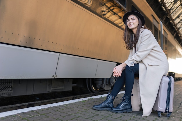 Chica sentada en la maleta esperando la salida del tren.