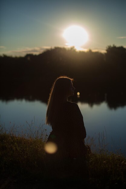 Foto chica sentada en la orilla del río.