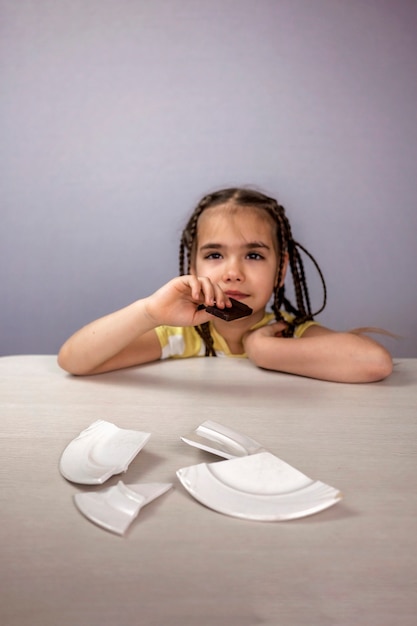 Chica sentada ante el plato roto y comiendo barras de chocolate con placer