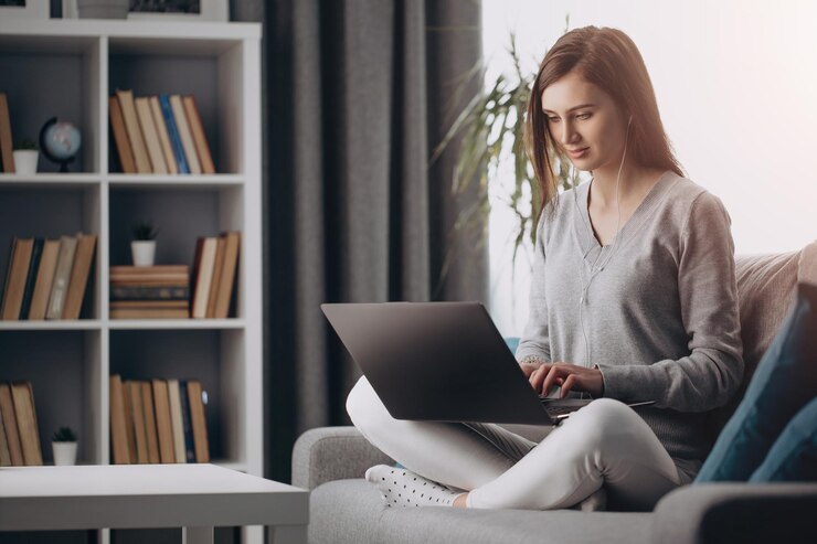 Chica sentada en un sofá con las piernas cruzadas y trabajando en una laptop