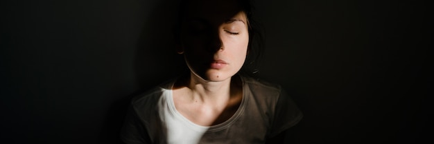 Chica sentada sola en el bolsillo de la luz del sol en el cuarto oscuro. concepto de salud mental