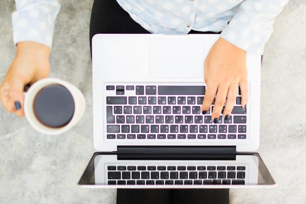 Chica sentada en el suelo con una laptop y una taza de café