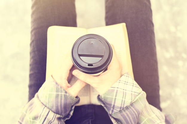 Chica sentada en el suelo con una taza de café y un libro.