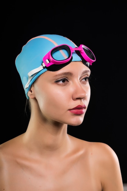 Una chica seria en un gorro de baño y gafas se prepara para nadar, piscina