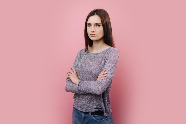 Chica seria de pie sobre fondo rosa con los brazos cruzados