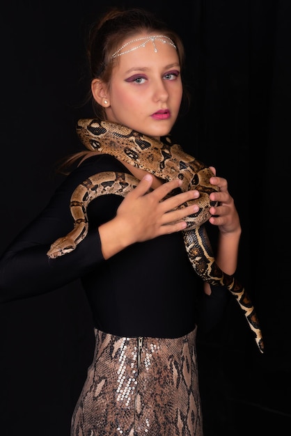 Foto chica con una serpiente en su cuerpo sobre un fondo negro