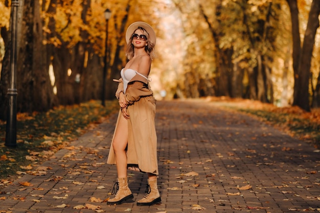 Chica sexy con abrigo y sombrero en un parque soleado de otoño