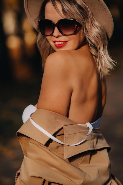 Chica sexy con abrigo y sombrero en un parque soleado de otoño