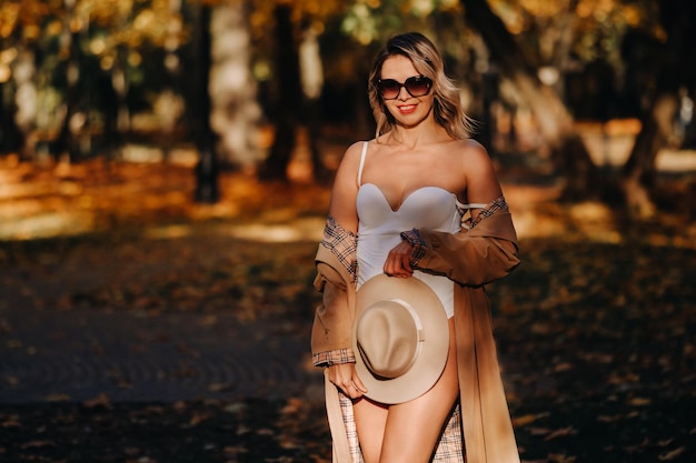 Chica sexy con abrigo y sombrero en un parque soleado de otoño