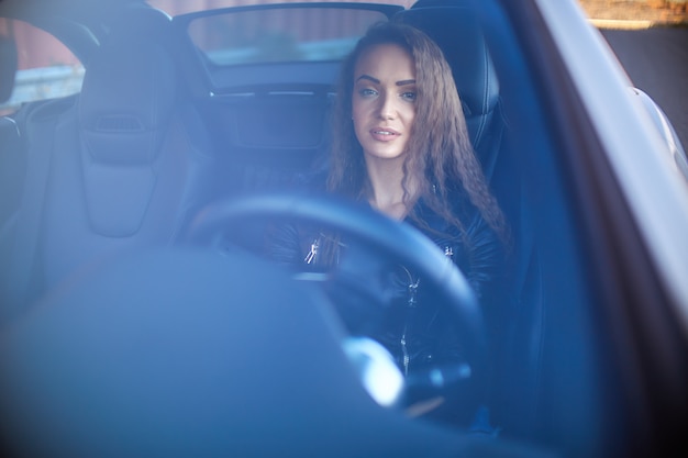 Chica sexy en una chaqueta de cuero, pantalones cortos de mezclilla y medias negras en la red se sienta al volante de un auto