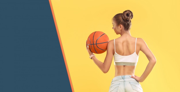 Chica sexy con shorts cortos sosteniendo una pelota de baloncesto en la pared amarilla
