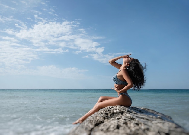 Chica sexy en traje de baño posa delgadamente sobre una roca blanca contra el fondo del mar