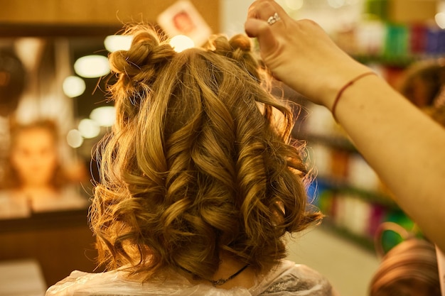 chica en una silla en la peluquería hace un peinado peluquero hace un rizo de pelo a una chica