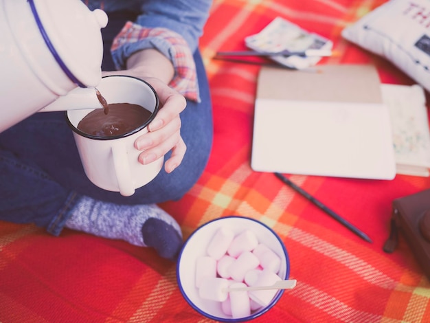 Chica sirviendo un chocolate caliente en un picnic con malvaviscos