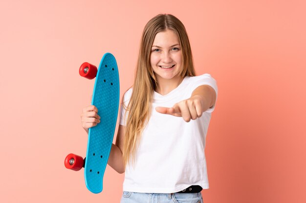 Chica skater ucraniana adolescente aislada en rosa con un patín y apuntando hacia el frente