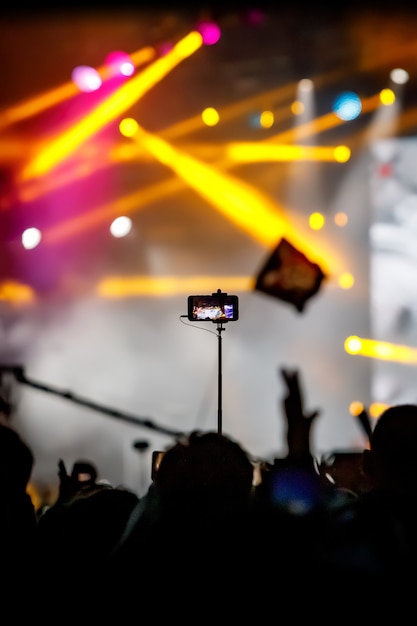 Foto chica con smartphone en trípode para tomar un video en un concierto.