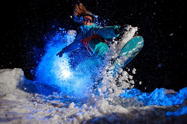 Chica de snowboarder vestida con una ropa deportiva naranja y azul realiza trucos en la nieve.