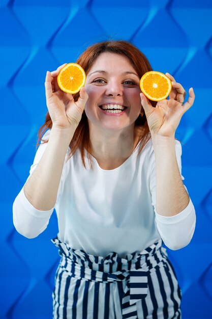 Chica sobre un fondo azul brillante en una blusa blanca con naranjas en la mano