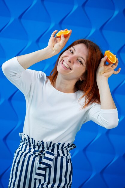 Chica sobre un fondo azul brillante en una blusa blanca con naranjas en la mano