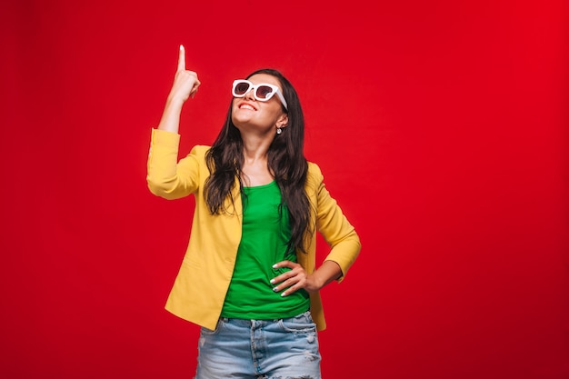 Chica sobre fondo rojo en chaqueta amarilla muestra los dedos en el espacio de la copia