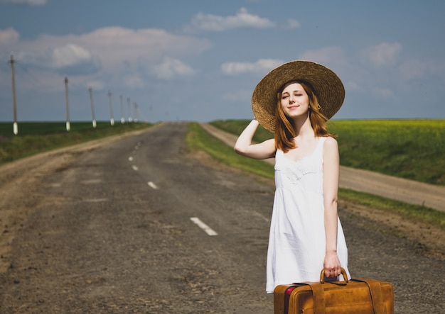 Chica solitaria con maleta en camino rural