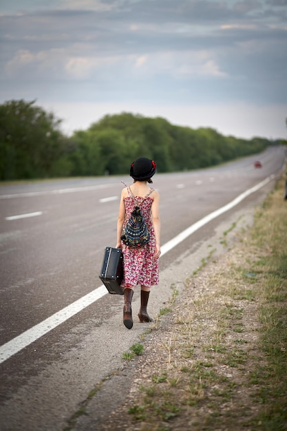 Chica solitaria con maleta de pie sobre la carretera