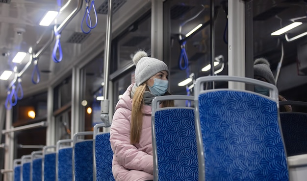 Chica solitaria con una mascarilla monta un tranvía por la noche en tiempo de pandemia