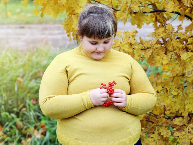 Chica solitaria obesa en ropa amarilla de pie al aire libre en otoño