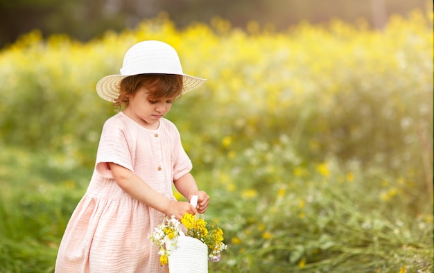 una chica con sombrero en el campo de colza con una cesta de flores