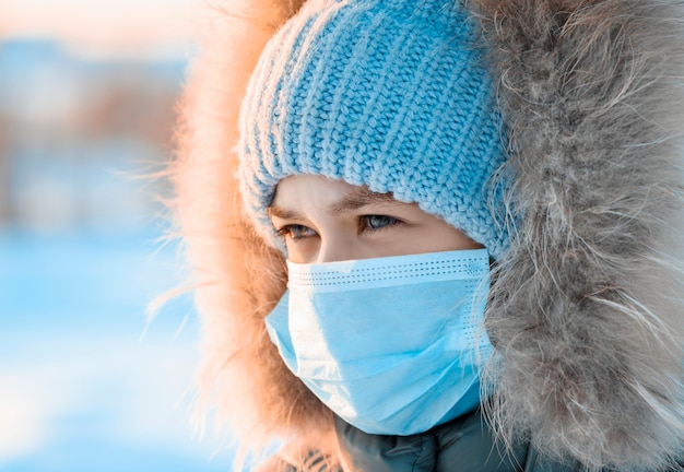 Chica con sombrero y capucha en máscara médica en el frío en invierno.