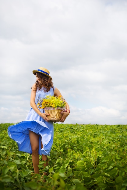 Chica en un sombrero se encuentra en un campo verde con una canasta de flores