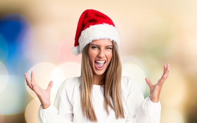 Chica con sombrero de Navidad infeliz y frustrada con algo sobre una pared desenfocada
