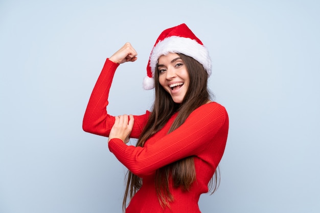 Chica con sombrero de Navidad sobre azul aislado haciendo gesto fuerte