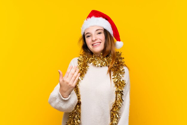 Chica con sombrero de Navidad sobre pared amarilla aislada invitando a venir
