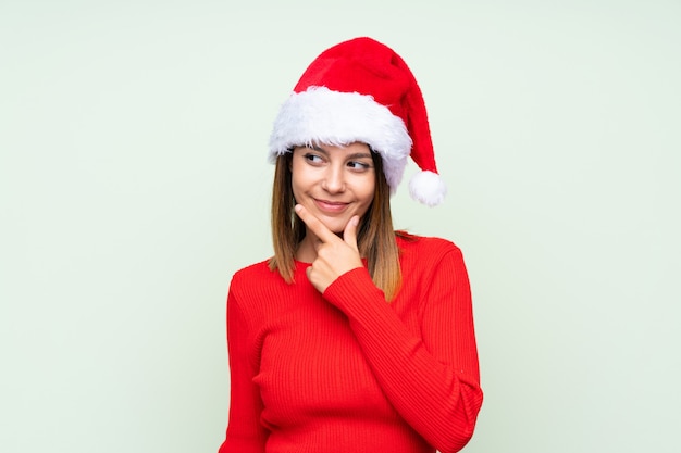 Chica con sombrero de Navidad sobre verde aislado pensando en una idea