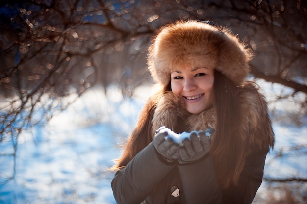 Chica con sombrero con orejeras soplando sobre la nieve.