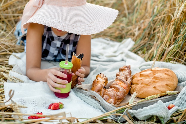 Chica con sombrero de paja en picnic.Vista superior. Picnic estético al aire libre con pan y fruta, bayas y croissants.