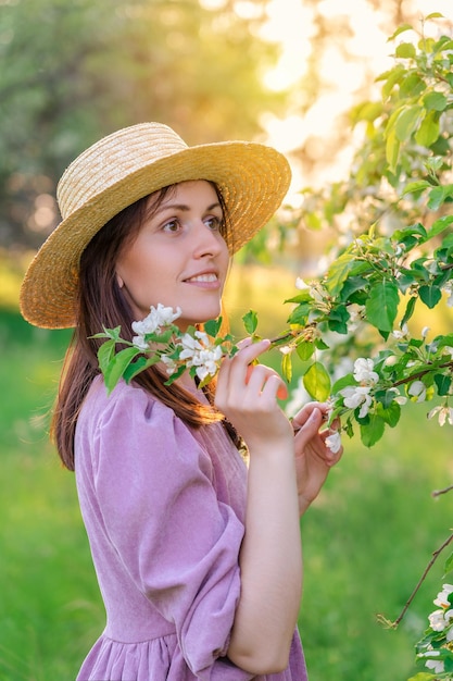 Una chica con un sombrero de paja posa en un huerto de manzanas