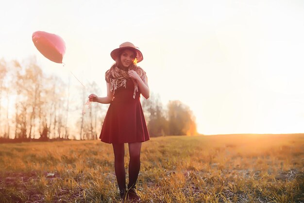 Una chica con sombrero en un paseo por el parque. Una niña con una canasta camina en otoño. Chica camina por la carretera al atardecer.