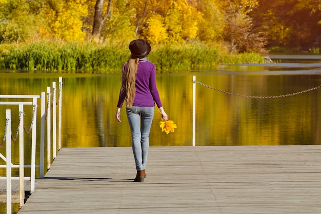 Chica con sombrero de pie en el muelle. Día soleado de otoño. Vista trasera